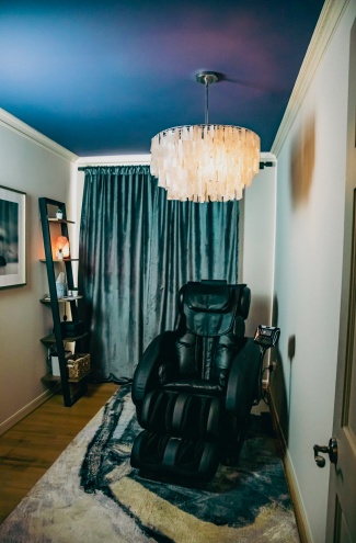 A relaxation room with a soft carpet beautiful modern chandelier and a centrally located massage chair